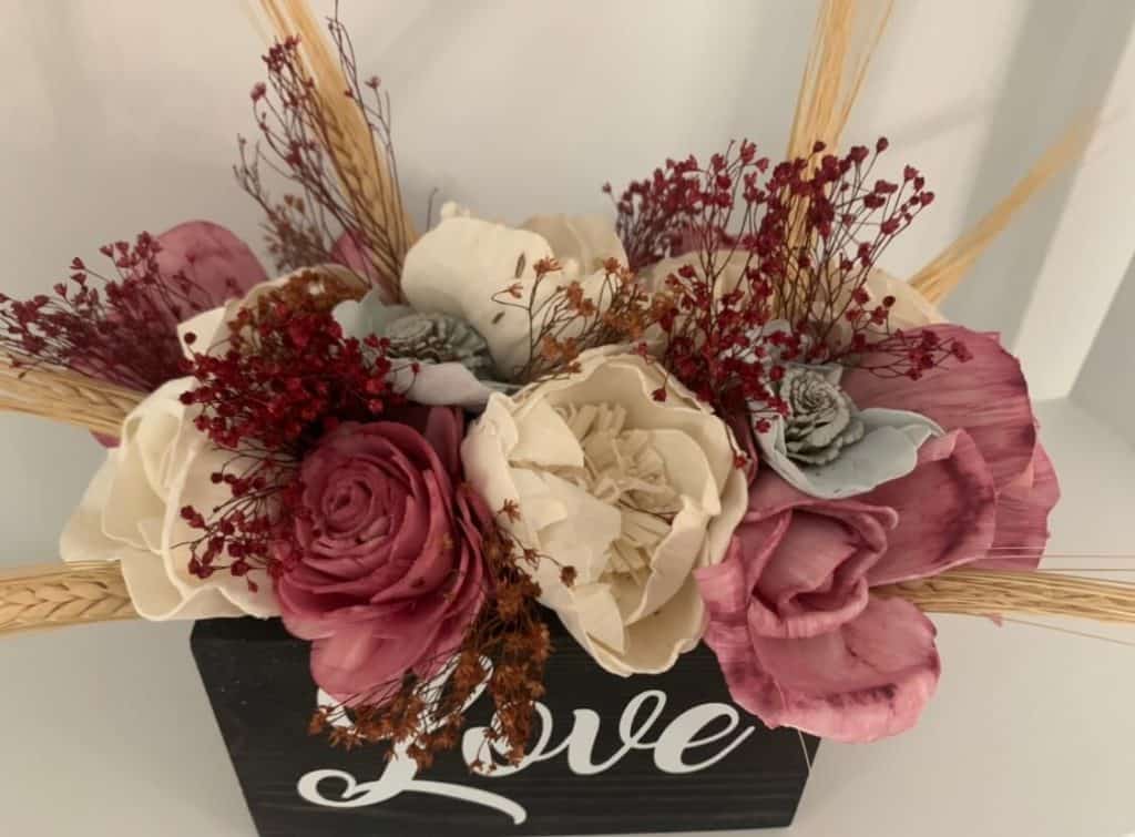 sola flower arrangement in black rectangular wood box.  Flowers in merlot, white and morning frost with burgundy and maroon filler and wheat filler.  The word Love is on the front of the rectangular box